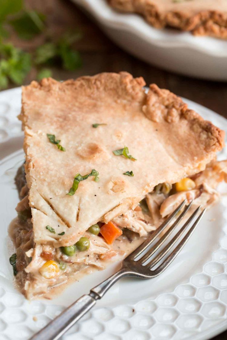 Uma fatia de torta de frango cheia de frango desfiado, legumes em um prato com um garfo.