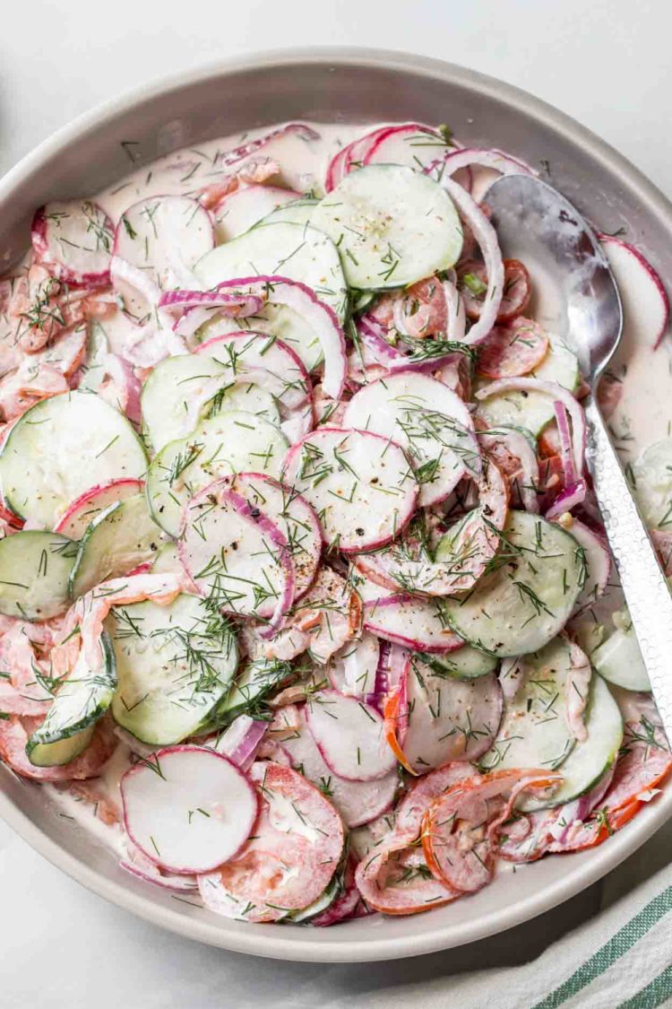 Salada de pepino e tomate em uma tigela com rabanete e misturada com um molho de maionese, coberto com endro fresco.