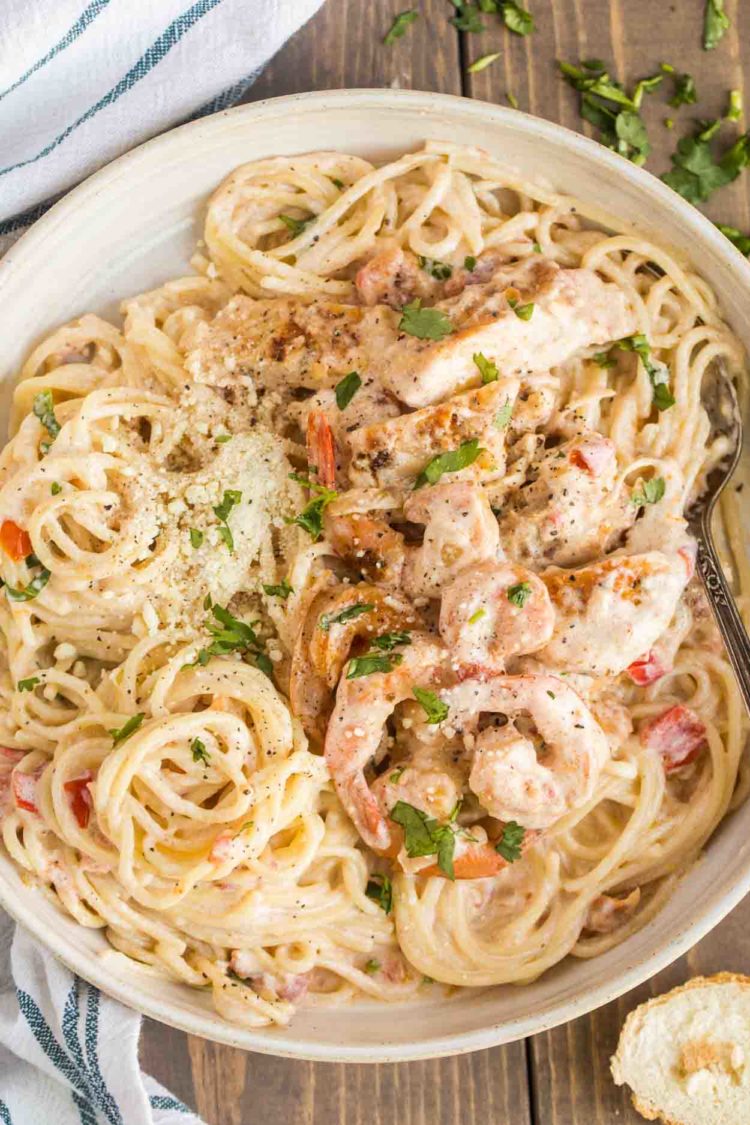 Frango cremoso à la carbonara e camarão em uma panela com uma colher coberta com legumes frescos.