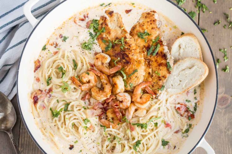 Uma panela com macarrão de galinha carbonara em uma panela com fatias de pão e legumes frescos.