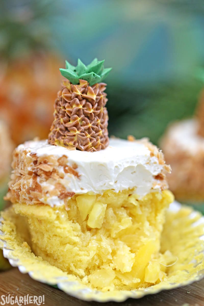 Cupcake de abacaxi com uma mordida e abacaxi fresco no meio, coberto com creme de coco | From SugarHero.com