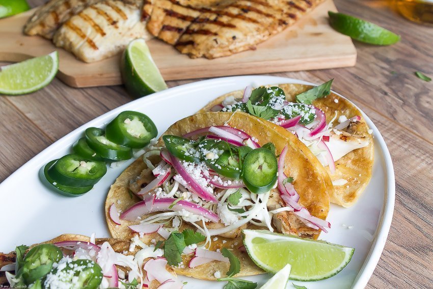 Tacos de peixe grelhado marinados em cerveja, esses tacos clássicos são cobertos com repolho ralado, rabanetes, cebola roxa em conserva, fatias de jalapeño e queijo cojita.