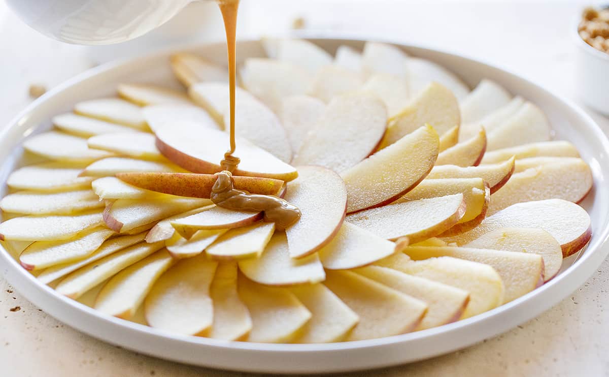 ¡Los Nachos de manzana con mantequilla de maní son la merienda perfecta después de la escuela! ¡Fácil de hacer, algunos ingredientes simples y MUCHAS caras felices! #applenachos #dessertnachos #afterschoolsnack #easyrecipes #kidrecipes #iambaker Manzanas rociadas con mantequilla de maní caliente