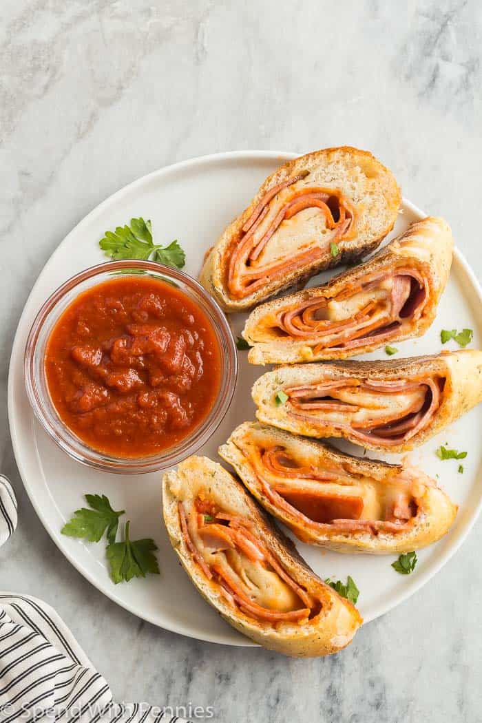 Fotografía cenital de 5 rodajas de stromboli en un plato blanco, con salsa marinara en un tazón y una toalla en el fondo