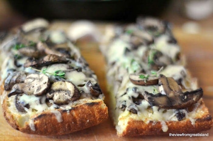 dos rebanadas de champiñones y Gruyere Bruschetta sobre una tabla para cortar madera
