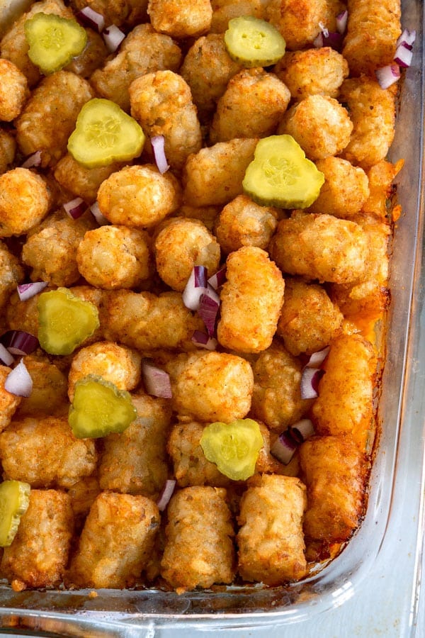 Tiro de arriba de cazuela de queso tater tot cubierto con pepinillos y cebollas