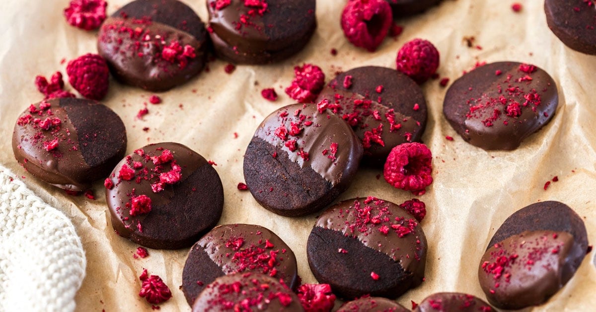 Un lote de galletas de chocolate negro, espolvoreadas con frambuesas liofilizadas en una hoja de papel de hornear marr&oacute;n