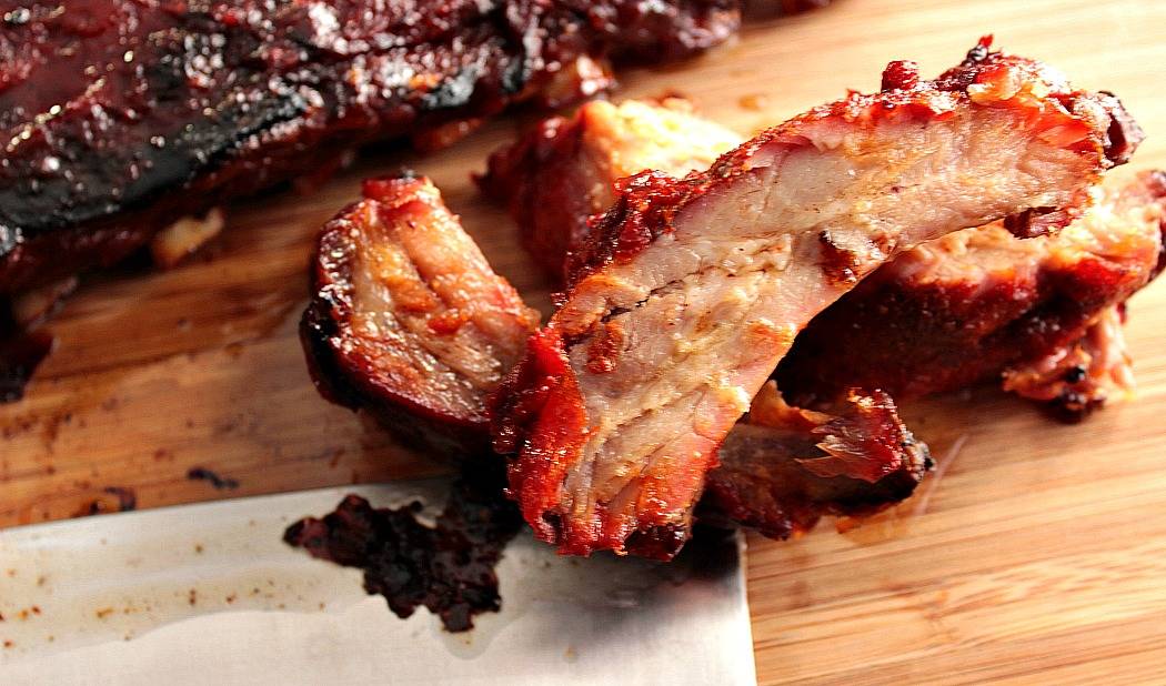 Closeup vertical photo of 3 baby back ribs on a wooden board with sauce.