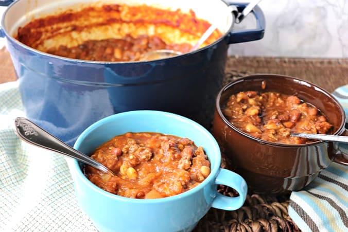 Two bowls of spaghetti squash chili in the foreground with a blue pot of chili in the background.