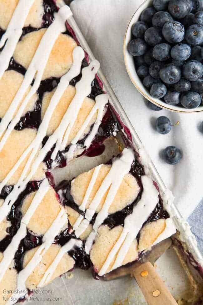 Overhead shot of Removing a Blueberry Pie Bar from the baking sheet and a bowl of blueberries