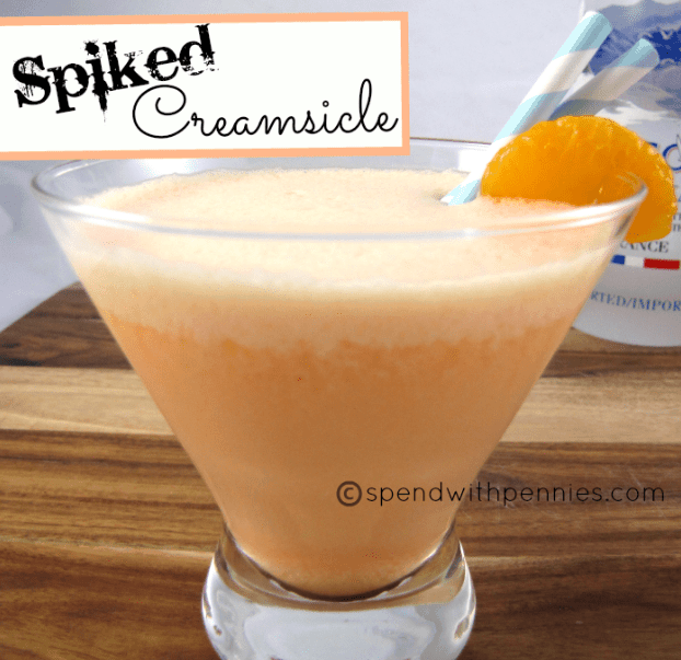 spiked creamsicle cocktail in a martini glass with vodka and oranges in the background