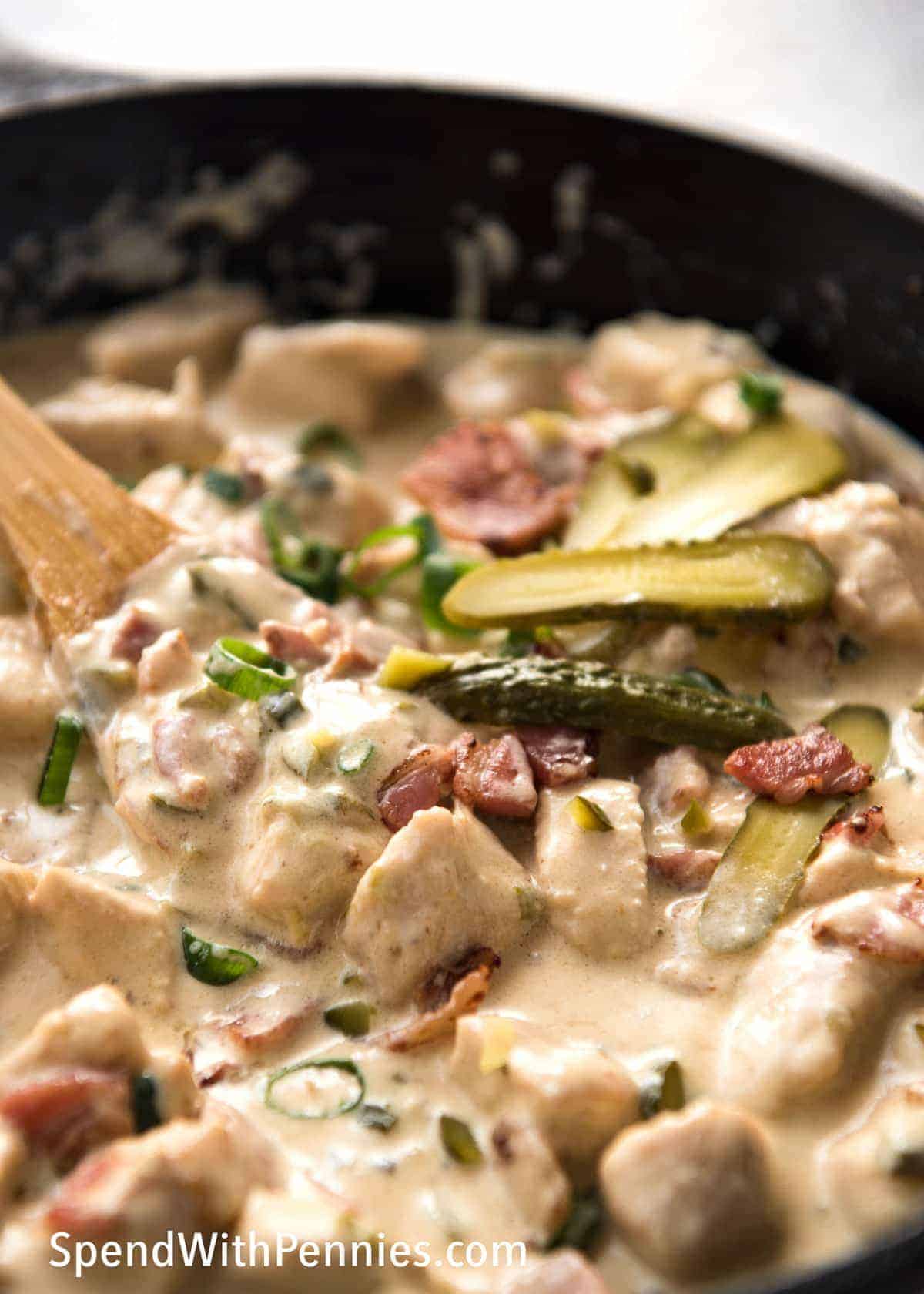 Stirring Dill Pickle Chicken with Bacon in a black pan with a wooden spoon