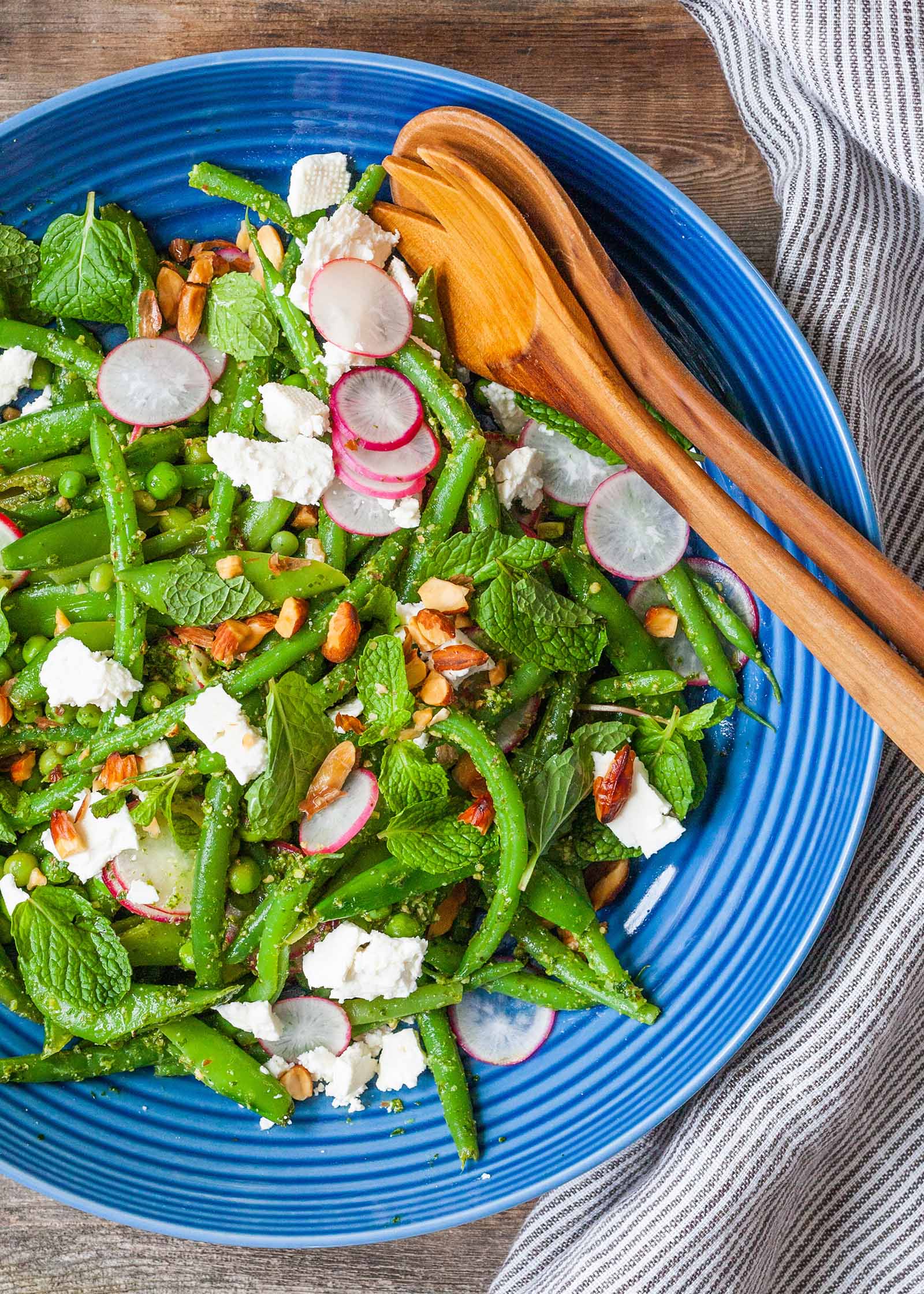 Easy Green Bean Recipe with Mint Pesto - blue bowl with a salad of green beans, radish, and wooden serving spoons on a wood table.