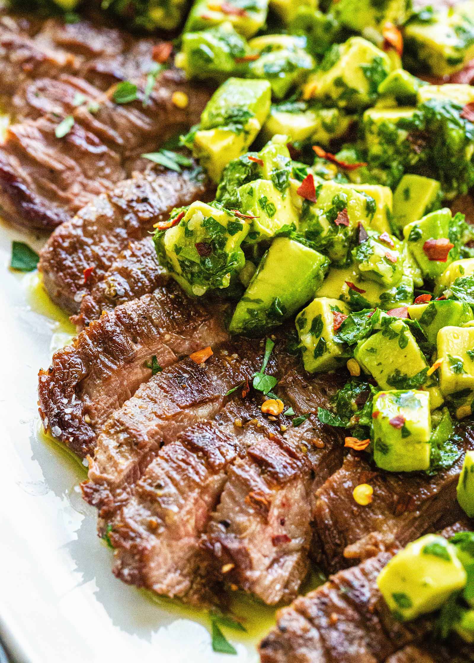 Quick and Easy weeknight skirt steak sliced across the grain and covered with avocado chimichurri on a white plate