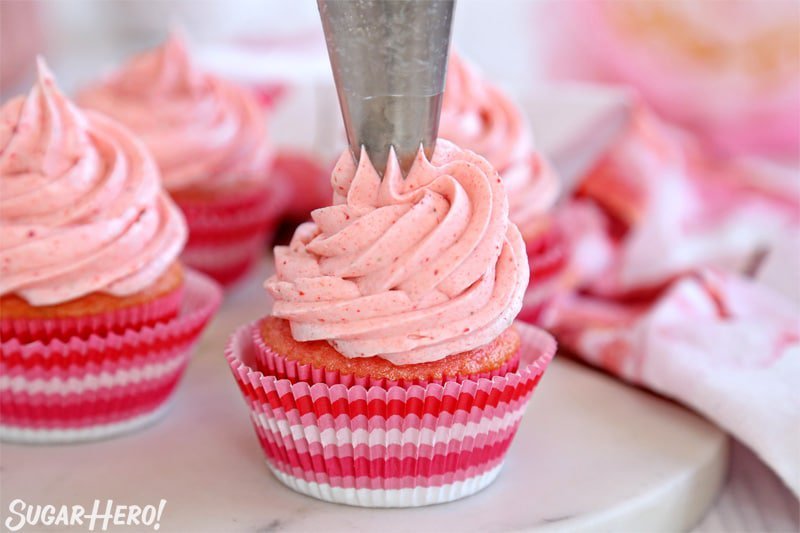 Glaseado de crema de mantequilla con fresas: un gran remolino de glaseado rosa encima de un pastelito | De SugarHero.com