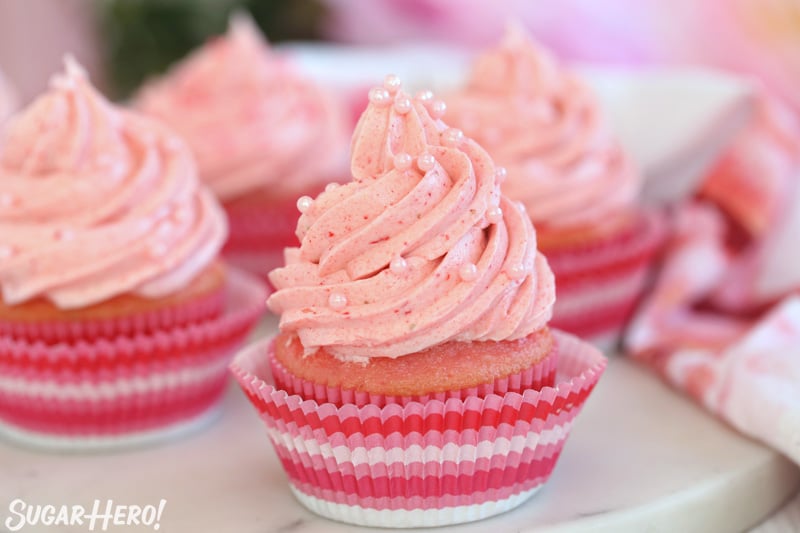 Glaseado de fresa y crema de mantequilla - magdalenas rosadas con glaseado de fresa y perlas de azúcar rosadas en la parte superior | De SugarHero.com