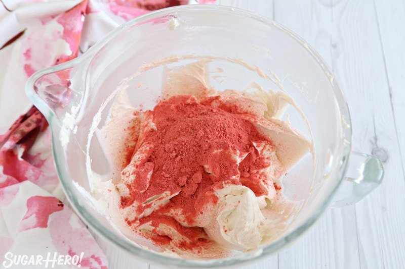 Glaseado de crema de mantequilla de fresa - polvo de fresa liofilizado esparcido sobre el glaseado blanco en un tazón | De SugarHero.com