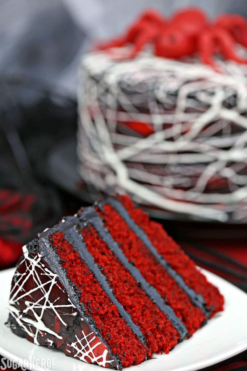 Red Velvet Marshmallow Spiderweb Cake - primer plano de la rebanada en primer plano con todo el pastel en el fondo | De SugarHero.com