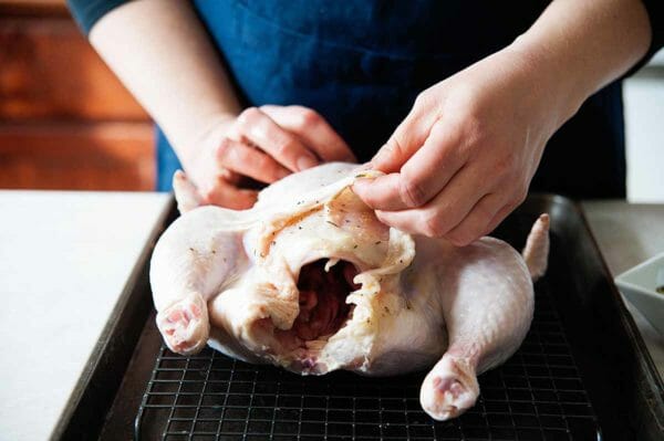 Cómo asar un pollo entero: mujer que separa la piel del pollo de la carne