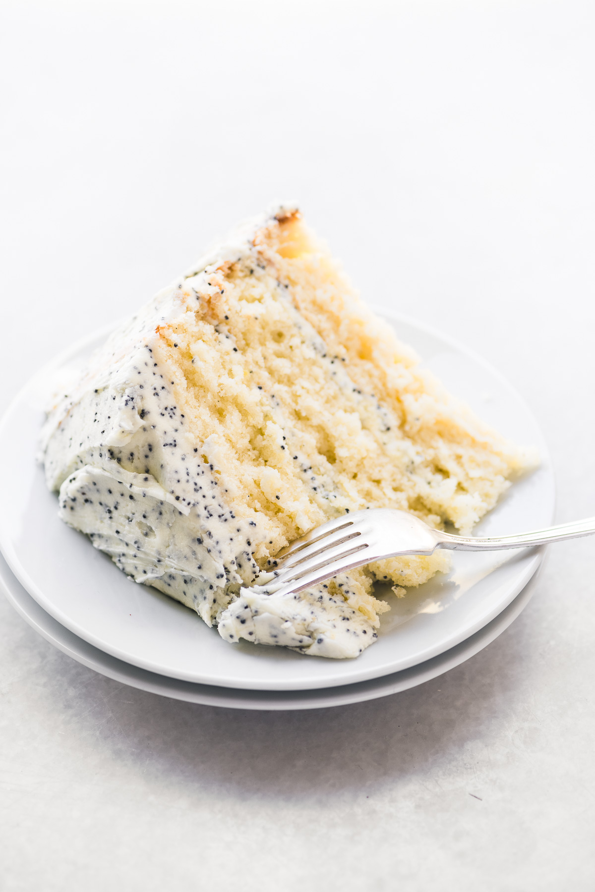 Una rebanada de pastel de limón con glaseado de crema de mantequilla de semillas de amapola, en un plato