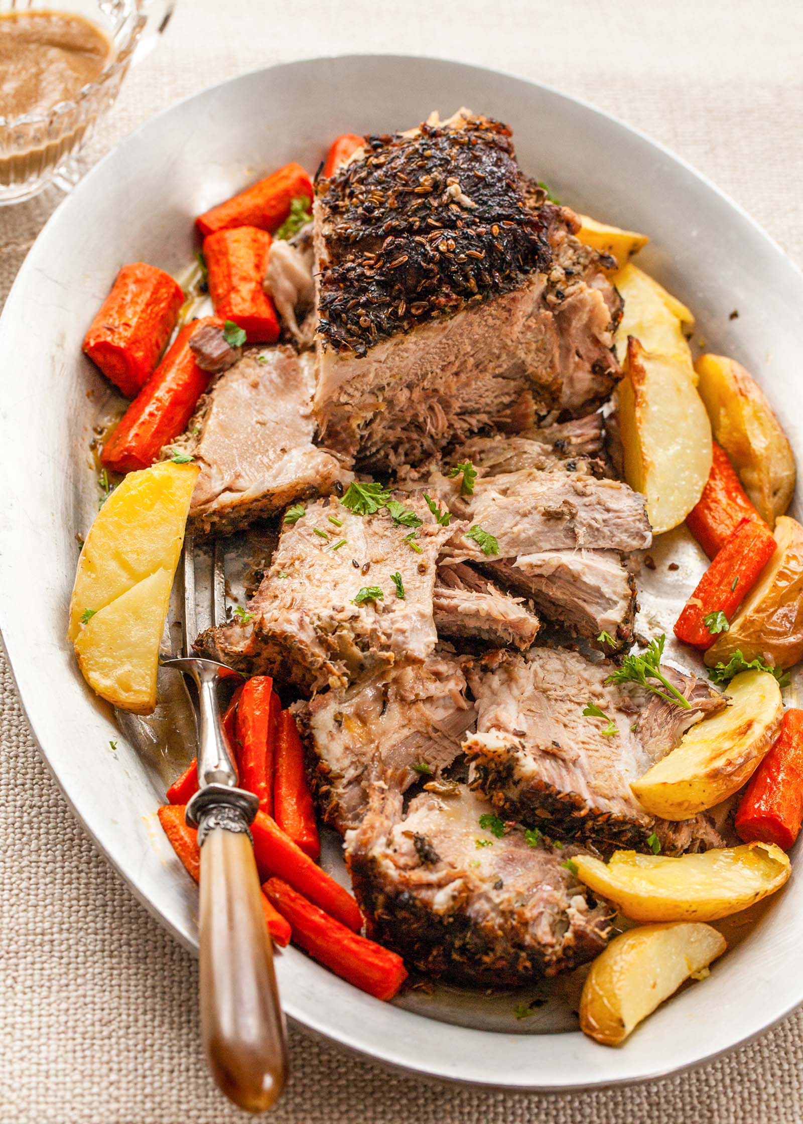 Sliced pork shoulder recipe served with roasted potatoes and carrots.