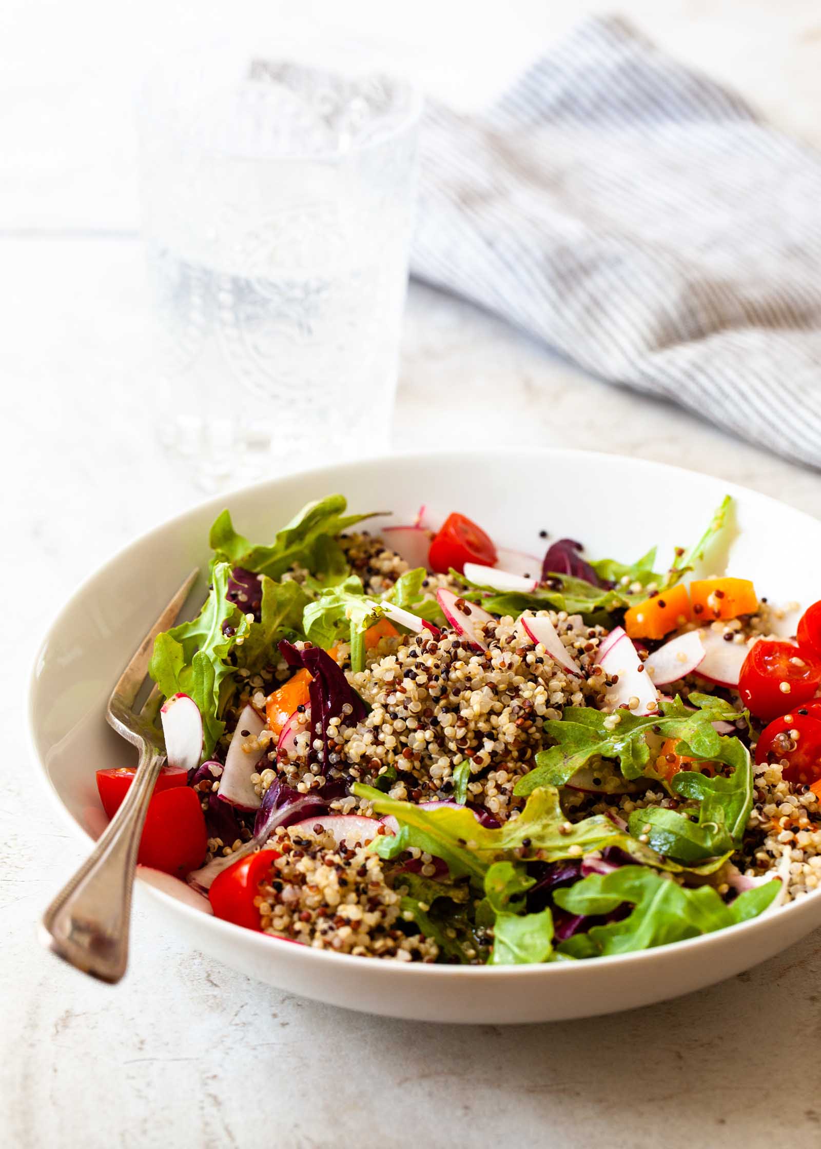 Perfect quinoa in a bowl along with lettuce, tomatoes, radish and a fork.