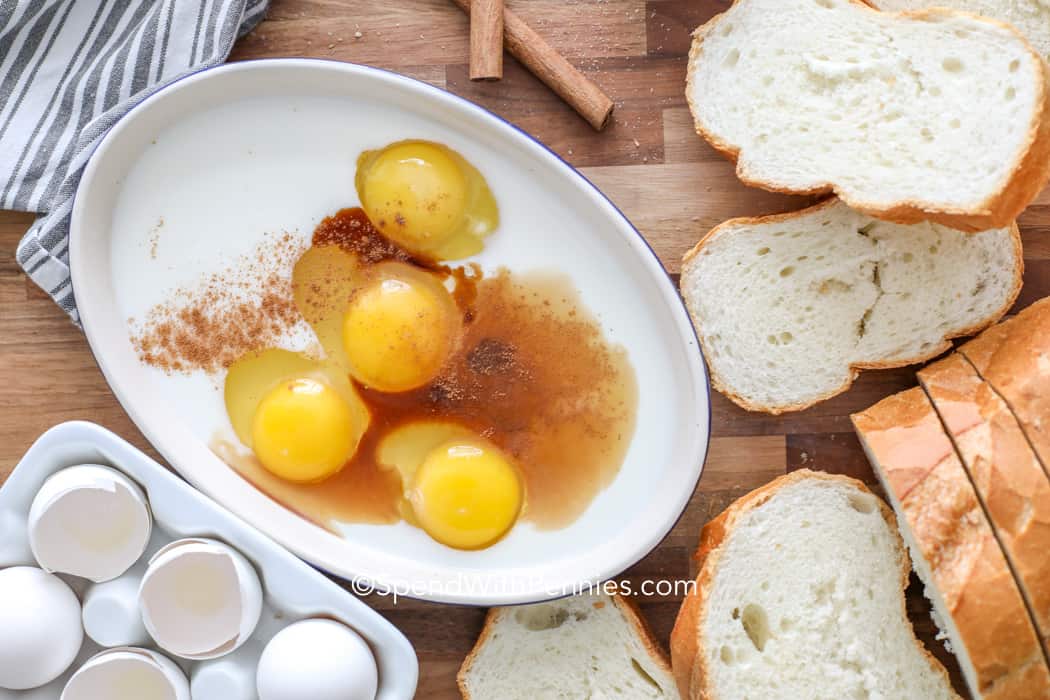 Huevos, leche y canela en un bol rodeado de pan y huevos