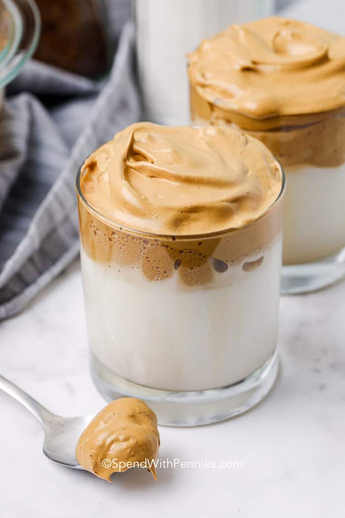A glass of milk topped with whipped coffee and a spoon of whipped coffee