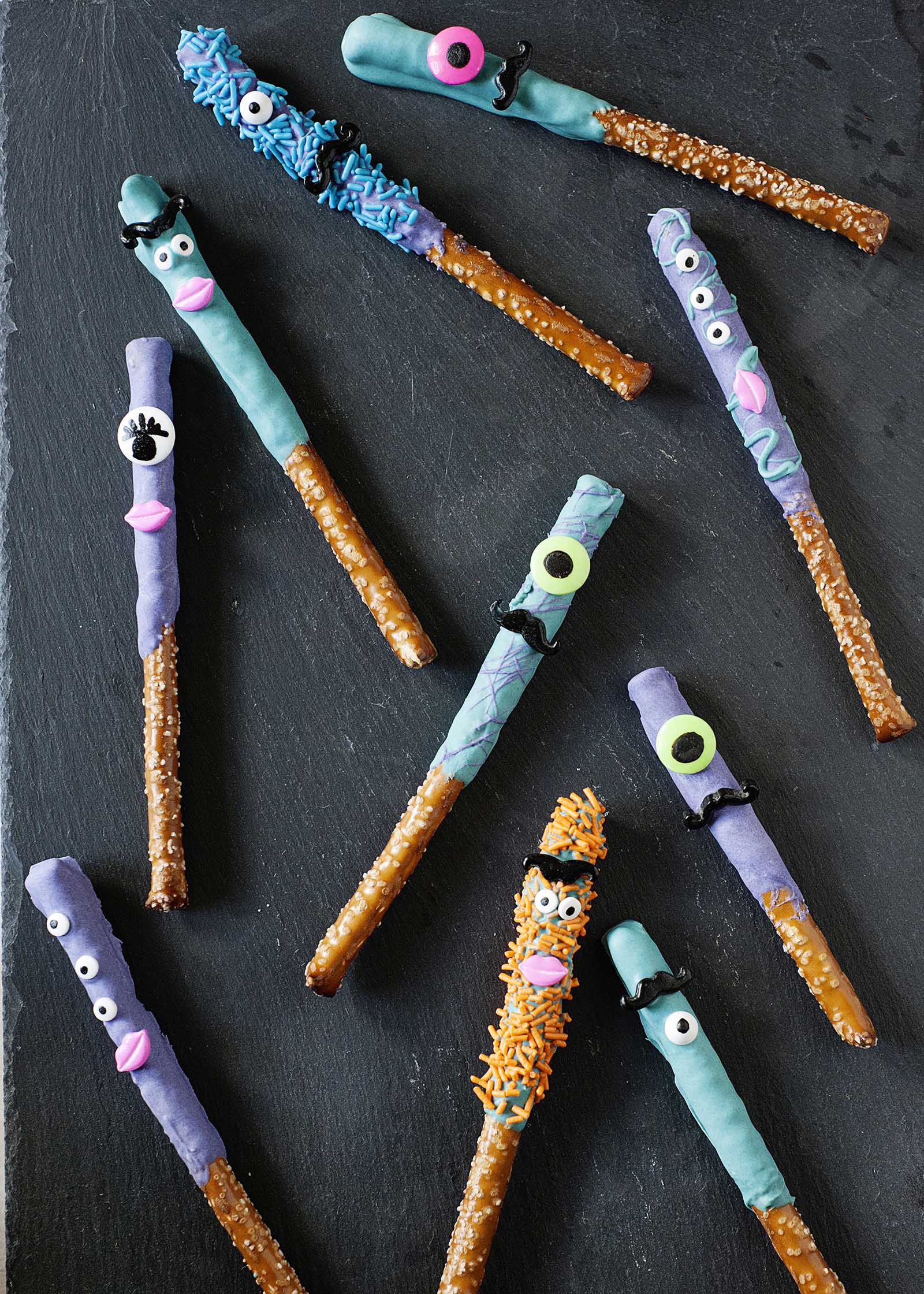 Homemade halloween-themed chocoalte covered pretzels decorated with eyes and lips on a dark gray background.