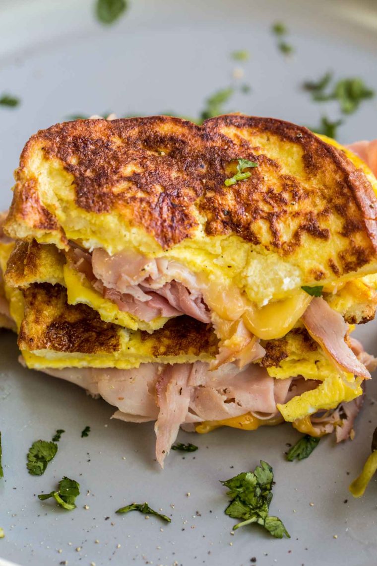 Receta de sándwich de desayuno con queso cargado de jamón en un plato cubierto con verduras frescas.
