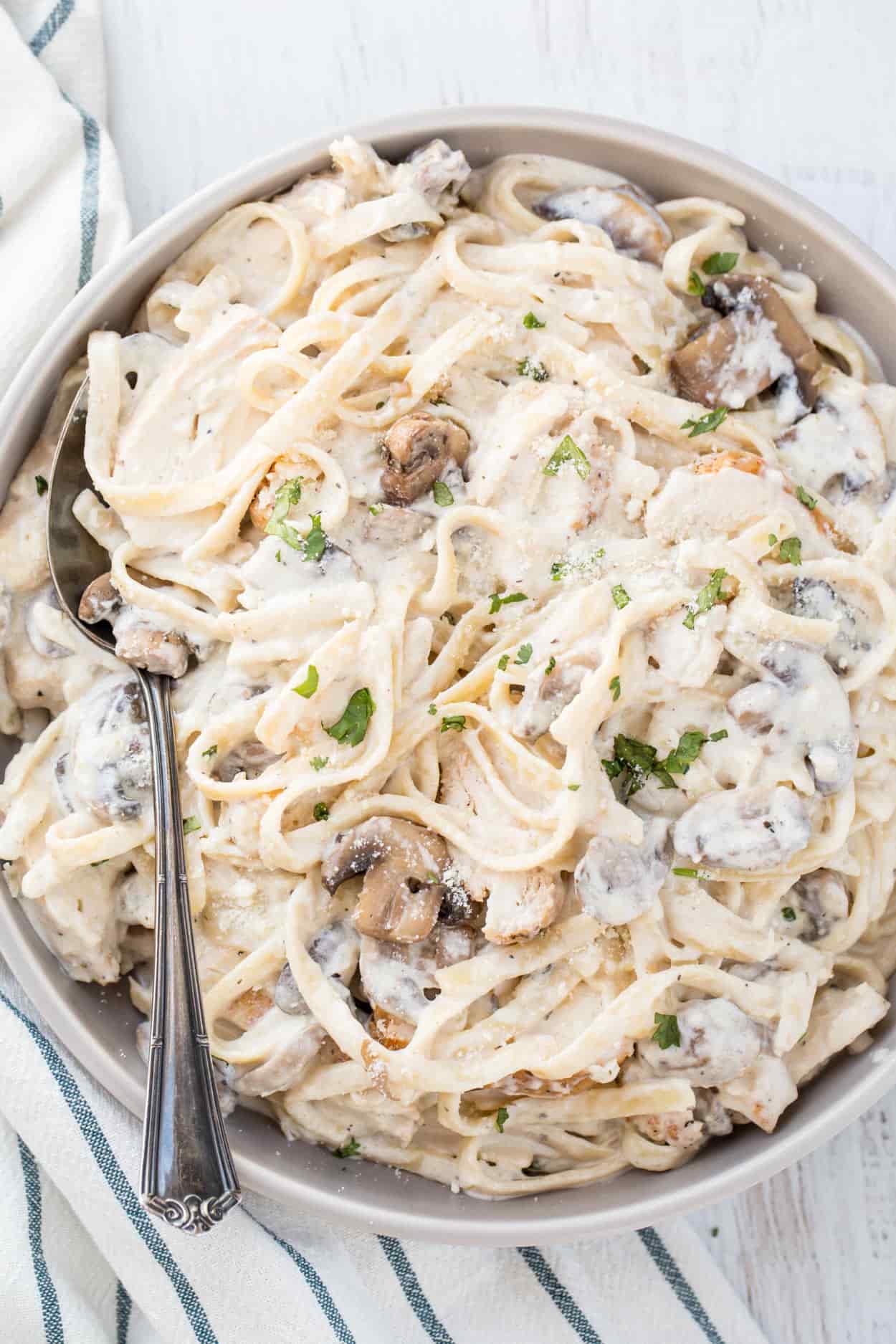 Chicken fettuccine Alfredo in a bowl with mushroom and fresh chopped herbs.