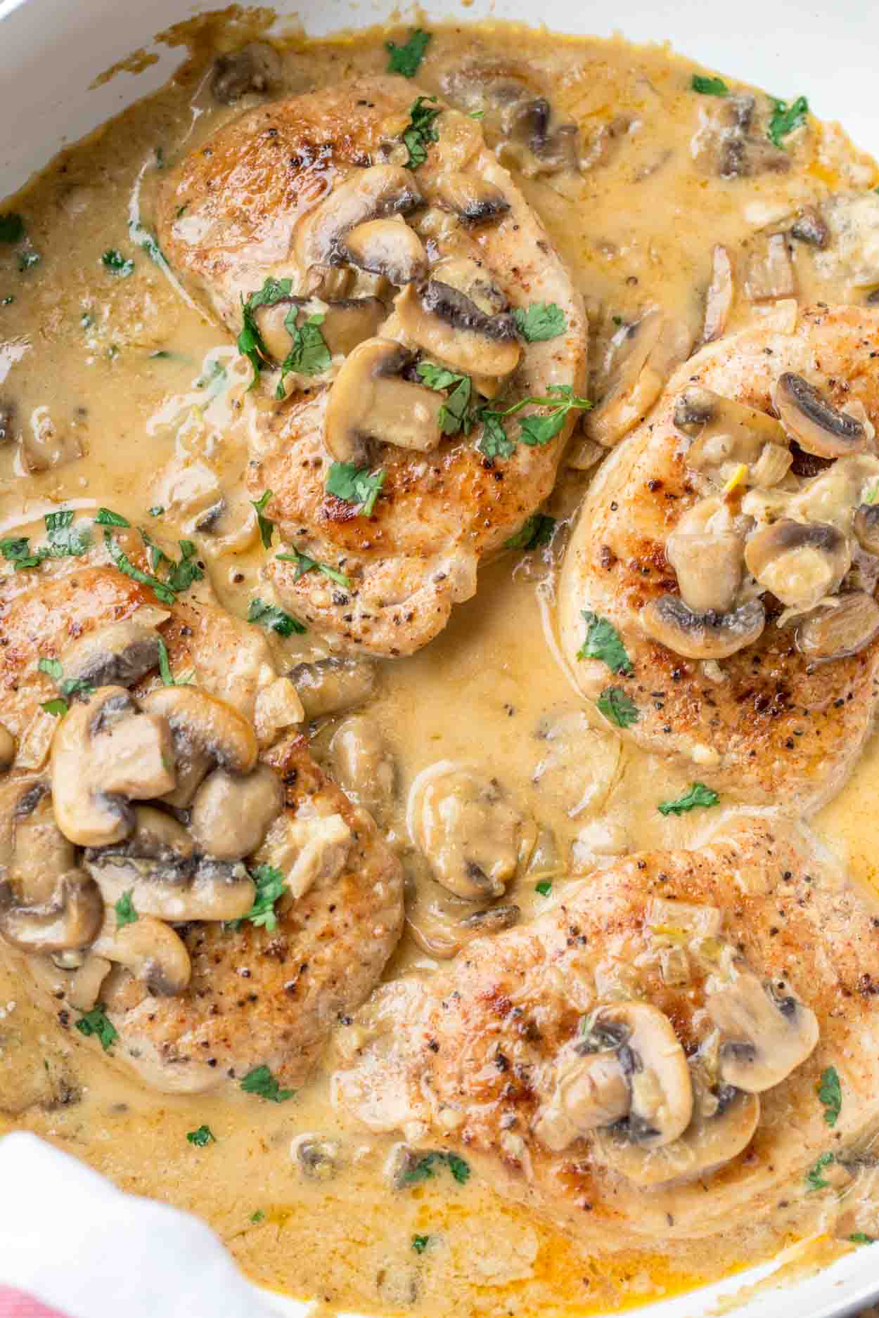 Pork chops in a skillet with a creamy mushroom sauce topped with fresh greens.