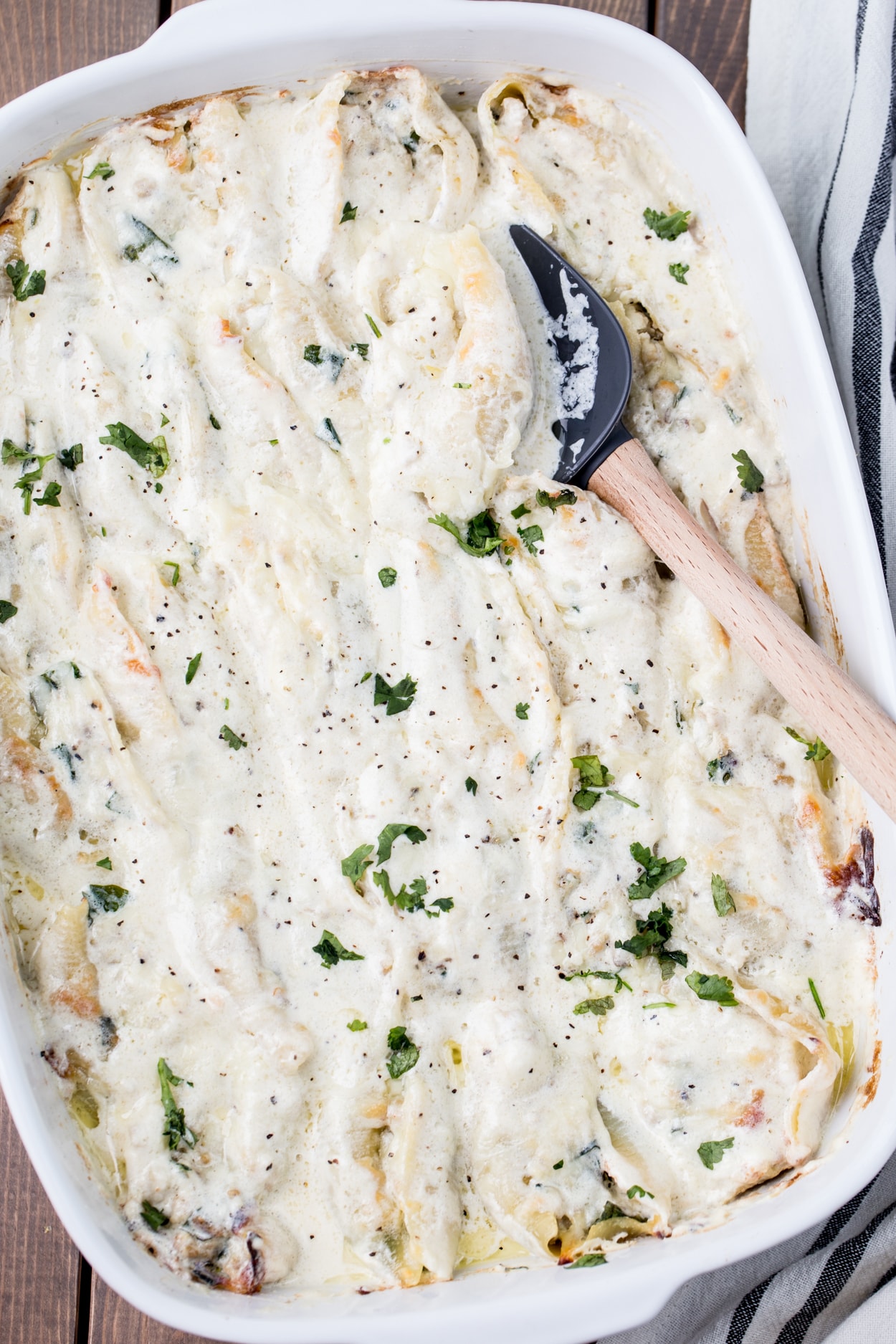 Chicken pasta shells in an Alfredo sauce in a casserole dish topped with fresh greens.