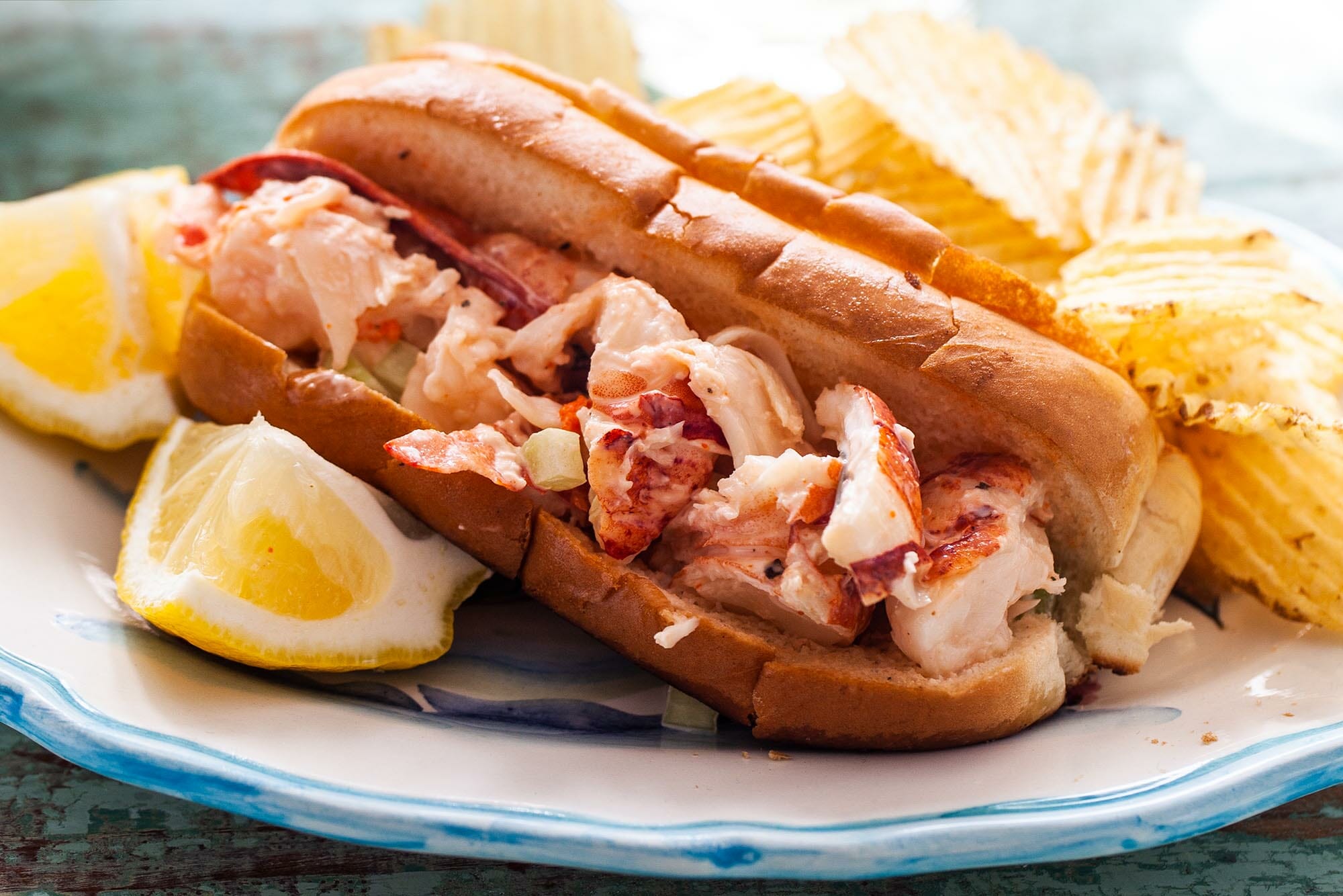 Plate of the best lobster roll recipe served with a side of chips and a lemon wedge.