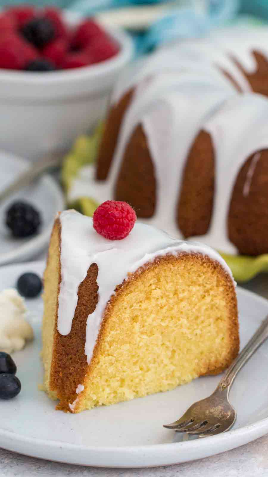 Slice of Vanilla Bundt Cake on white plate with berries and a fork