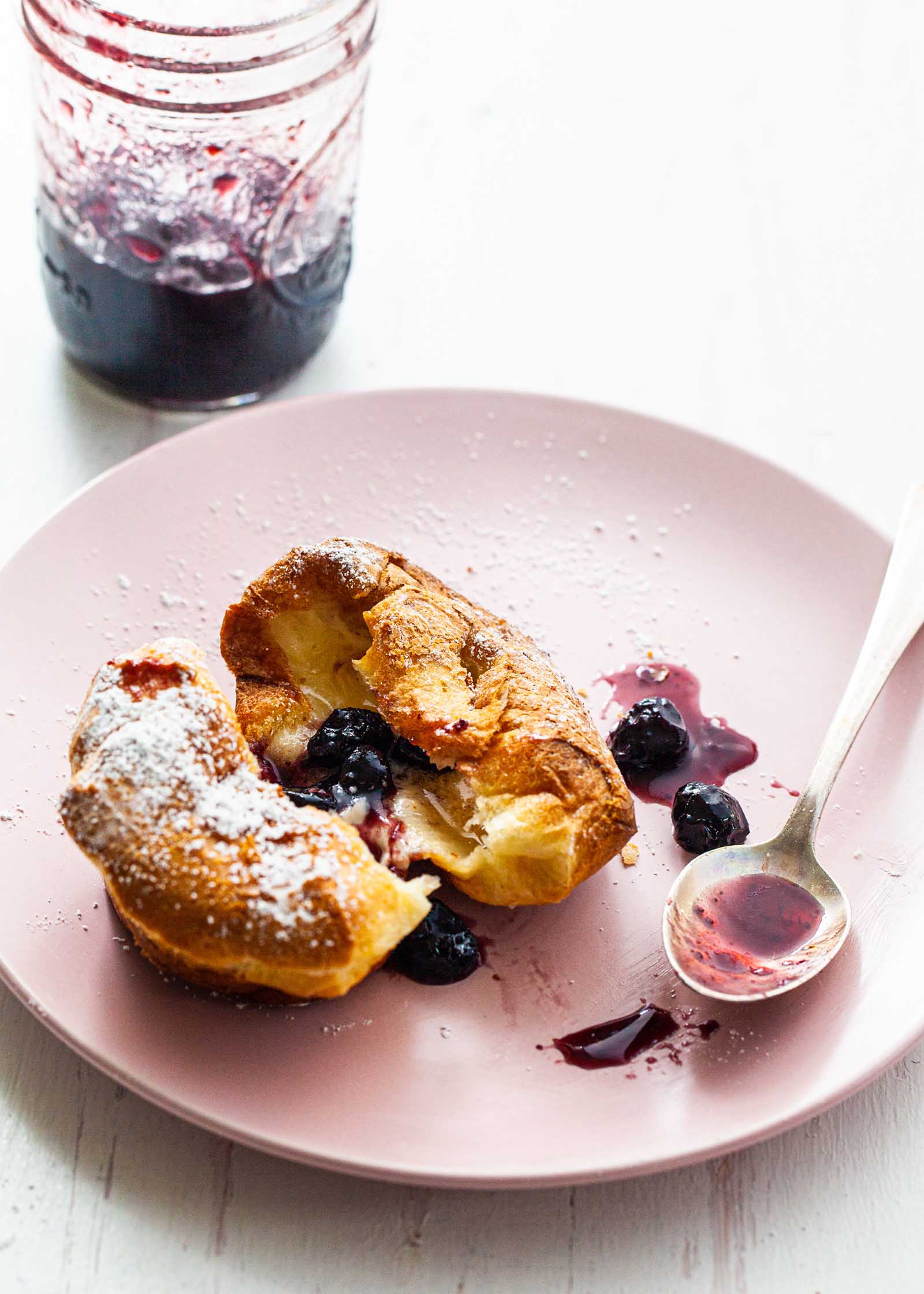 A popover split in half and spread with butter and jam.