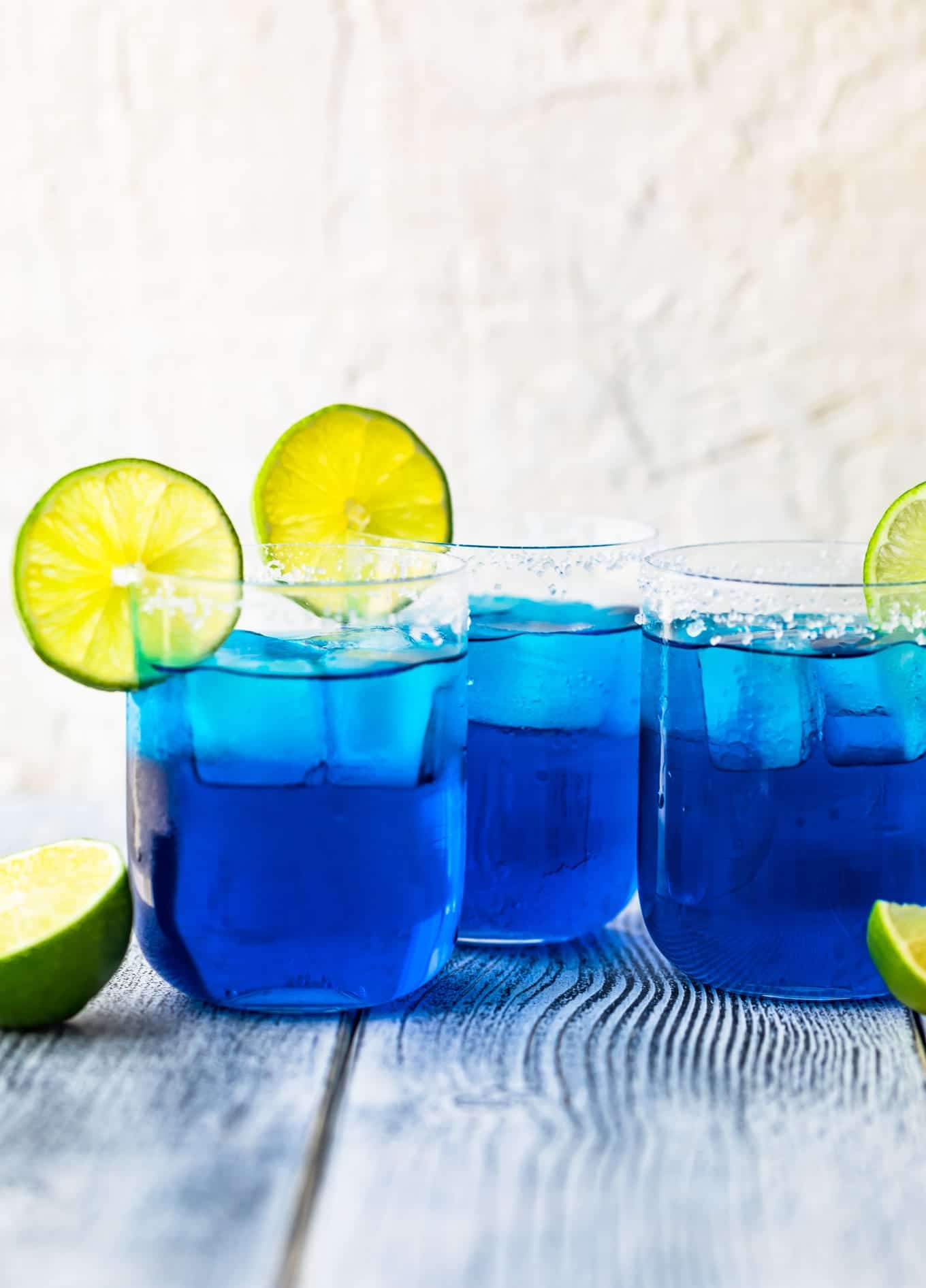 three blue margaritas in glasses topped with sliced limes