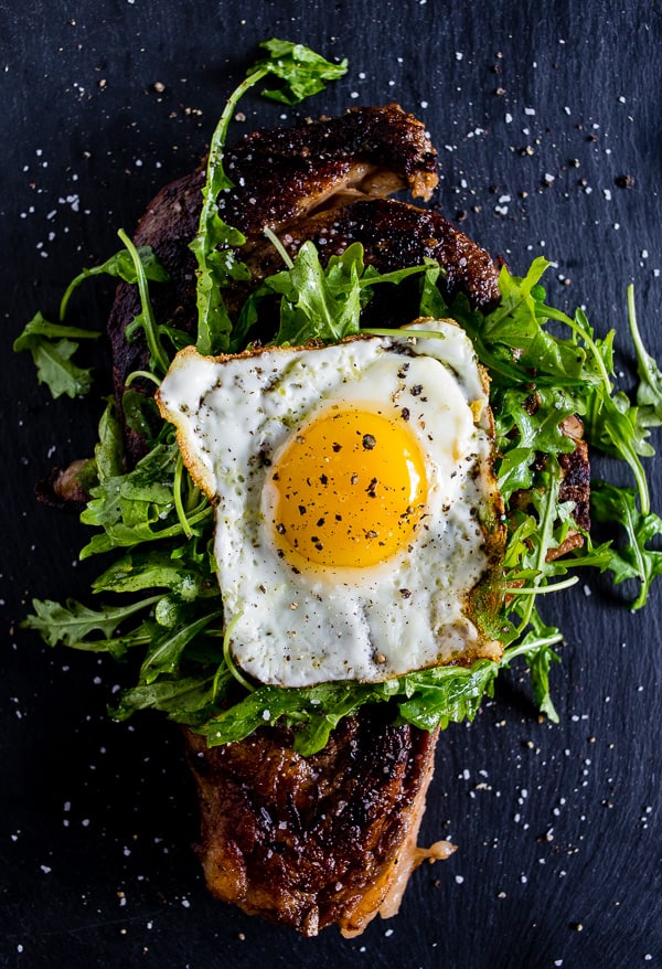 Fried egg sitting on top of arugula topped on a grilled steak