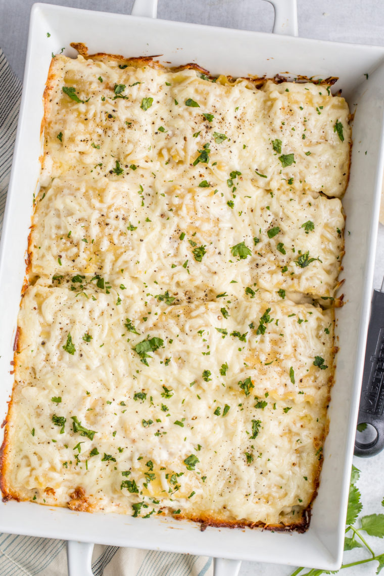 Chicken Alfredo Lasagna roll ups in a white casserole dish topped with fresh greens.