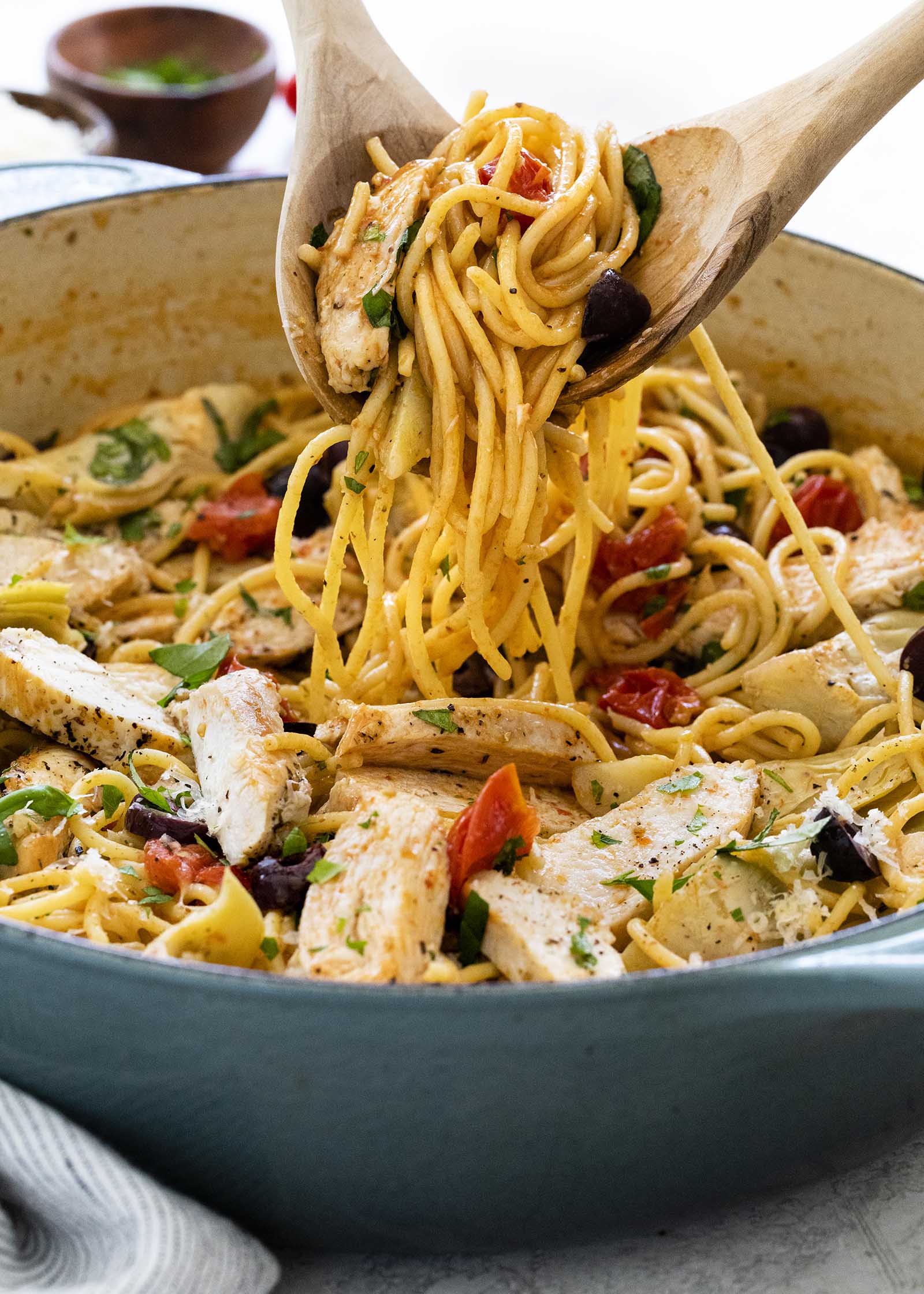 Two wooden spoons scoop easy chicken pasta skillet dinner out of a large skillet.
