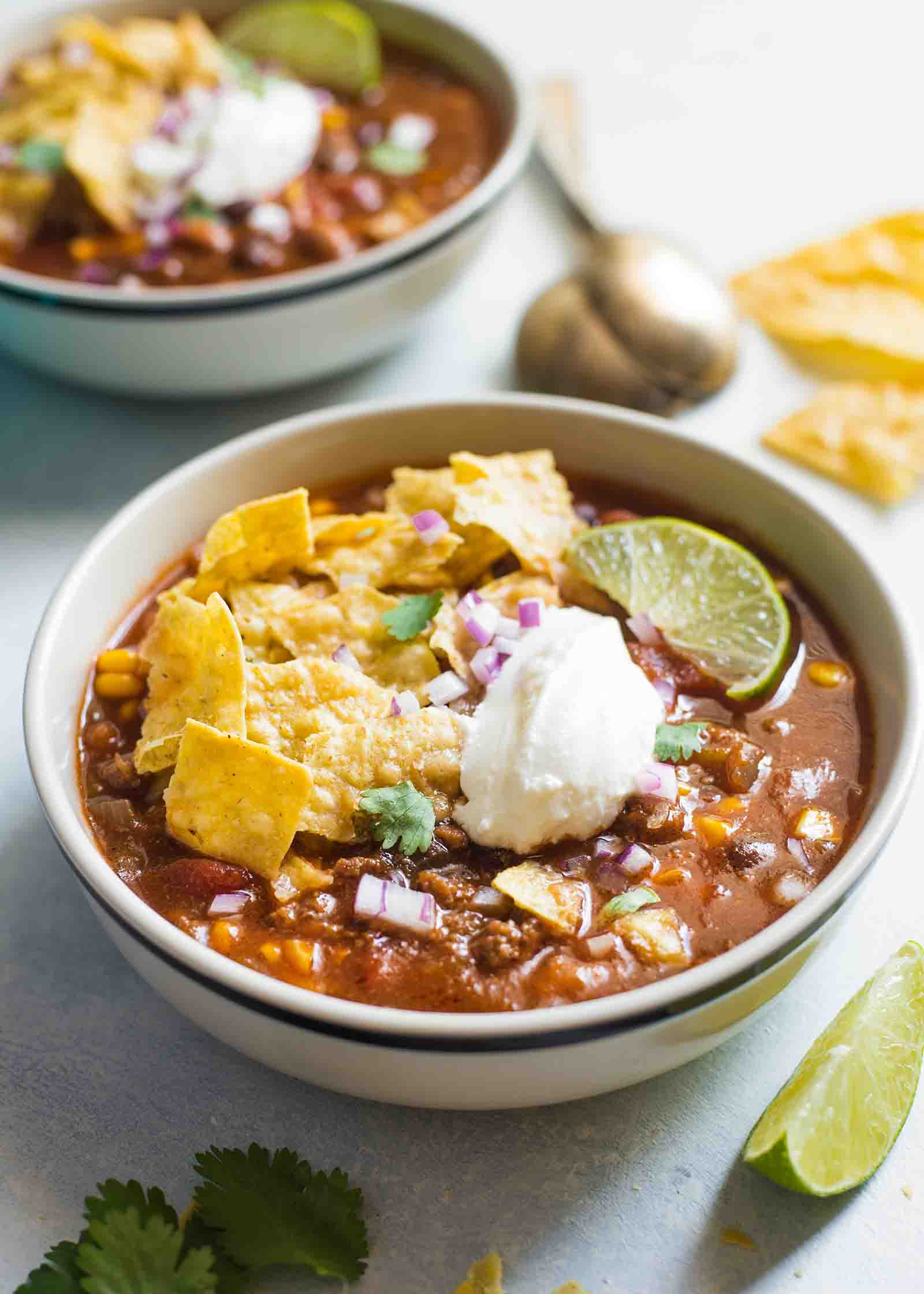 Crockpot taco soup made with beans, ground beef, beans, and corn, and topped with tortilla chips, sour cream, and lime wedges.