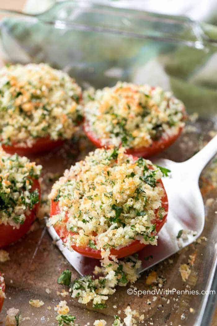 Oven Roasted Tomatoes in a clear baking dish, lifting one out with a spatula